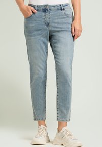 Jeans de mezclilla azul claro con un corte relajado, cinco bolsillos y puños. Llevados con zapatillas beige; presentan un desvanecimiento sutil.