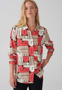 Overhemd met knopen en een geometrisch patroon in rood, beige, zwart en wit. Gemaakt van een gladde stof met lange mouwen en een kraag.