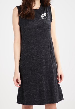 Femme portant une robe Nike gris foncé sans manches avec un logo blanc et le texte "Just Do It" sur la partie supérieure gauche de la poitrine.
