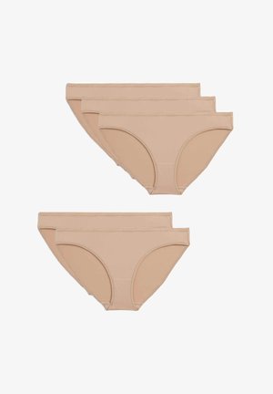 Débardeur blanc à côtes avec des bretelles larges, associé à des dessous beiges. La main du modèle ajuste la taille, fond neutre.