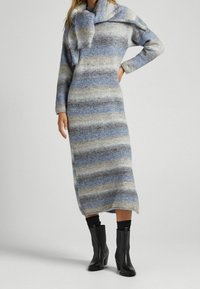 Abito di lana lavorato a maglia con strisce blu e beige, caratterizzato da un colletto alto e maniche lunghe, abbinato a stivali neri con tacco.