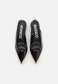 Ballerines noires en vernis avec un bride arrières, orteils pointus et bouts métalliques dorés. Elles présentent des semelles intérieures rembourrées, des intérieurs de marque et une finition lisse et brillante.