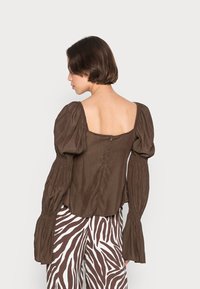 Blusa marrom de mangas bufantes com decote quadrado, apresentando tecido franzido, fecho de zip nas costas e material macio e texturizado.