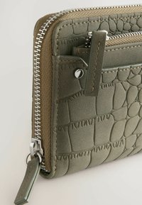Olivgrön plånbok med texturerad yta i krokodilsmönster. Har en silvrig dragkedja, tygdetaljer och flera kortfack.