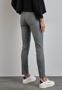 Ljust grå slim-fit jeans med midjehög midja, bakfickor och en mjuk textur, tillsammans med vita sneakers med marinblå detaljer.