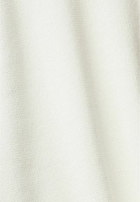 Gros plan sur un tissu couleur crème avec un tissage subtilement texturé et des plis doux créant des ombres douces.