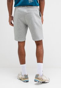 Grijze katoenen shorts met een elastische tailleband, zijzakken en een achterzak. Draagt lichte sneakers en witte sokken.