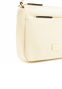 Borsa a tracolla in pelle beige con superficie testurizzata, hardware dorato e due tasche con zip nera sulla parte superiore. Logo in rilievo sul davanti.