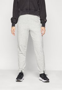 Grå joggebukser med elastiske mansjetter og snor i livet. Kombinert med svarte joggesko med hvite såler og teksturerte detaljer.
