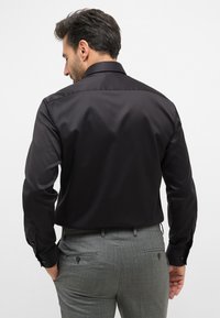 Zwart, lang mouw shirt met een soepele textuur, voorzien van een standaard kraag, knoopmanchetten en een getailleerd ontwerp, gecombineerd met grijze broeken.