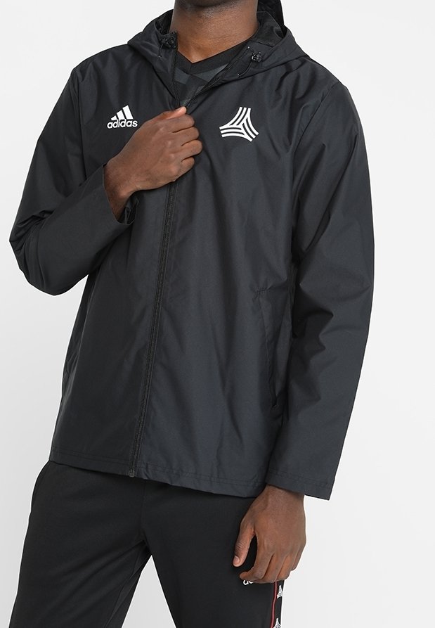 Czarna kurtka przeciwwiatrowa z kapturem, zapinana na przedni zamek, z bocznymi kieszeniami oraz białym logo Adidas na klatce piersiowej. Lekki materiał.