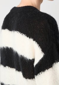 Sweter w czarno-białe paski, dziergany, wykonany z miękkiej, fakturowanej przędzy, z okrągłym dekoltem i widocznymi luźnymi nitkami wzdłuż pasków.