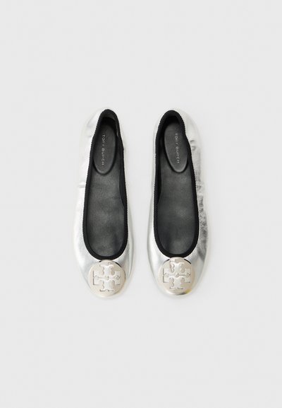 Une paire de ballerines Tory Burch en argent avec des bordures noires et un détail de logo métallique rond sur le bout, vue de dessus sur un fond blanc.