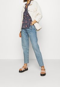 Veste en denim blanche, blouse florale marine, jean droit bleu clair et sandales à fines lanières roses avec semelles compensées noires.