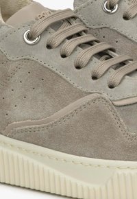 Grijze suède sneaker met beige accenten, gevoerde kraag en een gestructureerde rubberen zool. Voorzien van platte veters en contrasterende stiksels voor extra detail.