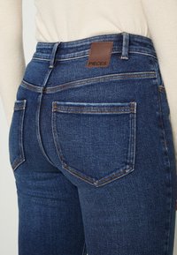 Jeans i denim med mörk tvätt och en klassisk femfickorsdesign. Har en brun läderlogga ovanför den högra bakfickan.