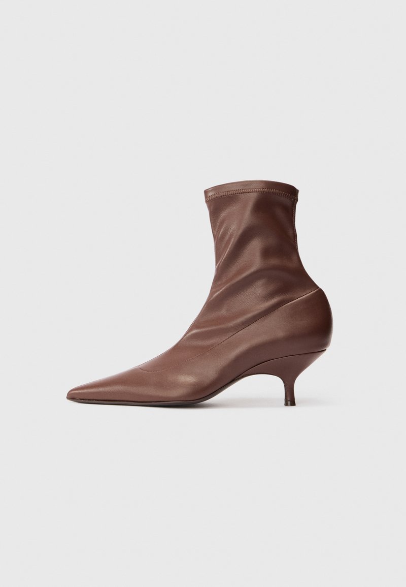 Bottine marron à bout pointu avec un talon kitten de hauteur intermédiaire et une tige en cuir doux et lisse sur fond clair.