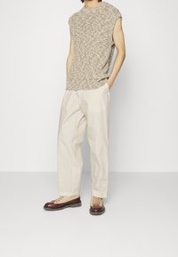 Lyhythihainen beige neulepaita, kermaiset leveälahkeiset housut ja ruskeat nauhaketjut, joissa on punaisia yksityiskohtia. Yksinkertainen, tekstuurinen muotoilu ja rento istuvuus.