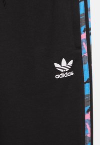 Black sweatpants featuring a blue, pink, and grey patterned side panel and a white adidas logo on the lower part. Soft fabric texture.