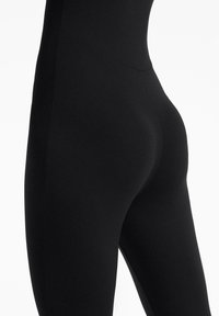 Gros plan sur une personne portant des leggings noirs moulants, mettant en valeur la coupe et le tissu lisse sur les hanches et les cuisses.