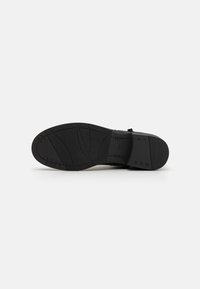 Suela de zapato de goma negra con superficie texturizada, que presenta un área central lisa y nervaduras en relieve para mejorar el agarre. El tacón está ligeramente elevado.