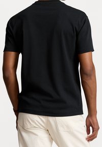 Černé bavlněné tričko s krátkými rukávy, kulatým výstřihem a hladkým povrchem. Na zadní straně se nachází jednoduchý, minimalistický design.