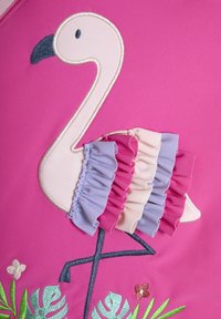 Vaaleanpunainen kangas, jossa on brodeerattu flamenco sinisellä nokalla, korostettuna vaaleanpunaisilla, laventelinvärisillä ja kermanvärisillä röyhelökerroksilla. Brodeeratut lehdet alapuolella.