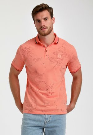Polo de color durazno con una textura de patrón sutil, de manga corta y un cuello que presenta una franja negra en contraste.