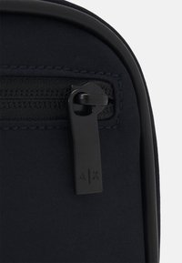 Borsa in tessuto color navy con superficie testurizzata, dotata di una cerniera nera e di una linguetta. Accentata con un logo minimalista sulla cerniera.