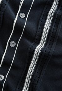 Navy blue knitted fabric with vertical white stripes and three gray buttons aligned in a row on the left side.