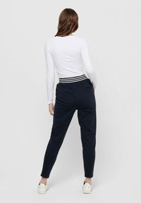 Marineblaue Jogginghose mit tailliertem Schnitt, ausgestattet mit einem strukturierten Bund mit weißen Streifen. Kombiniert mit einem taillierten weißen Langarmoberteil.