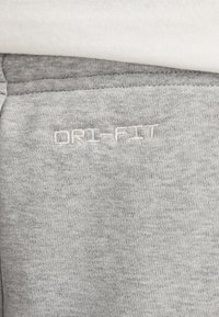 Grå Dri-FIT stof med en glat tekstur; har et hvidt broderet "DRI-FIT" logo. En del af sportstøj, der viser en blanding af stilarter.