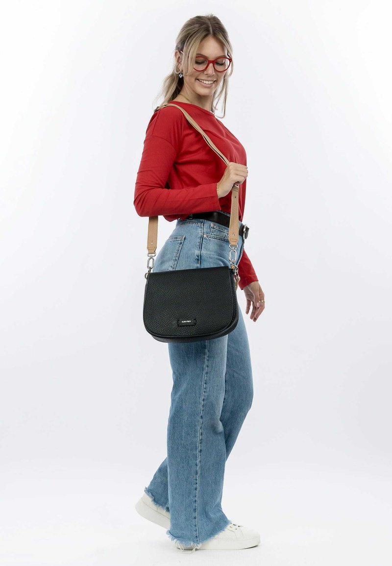 Black leather crossbody bag with a textured surface, featuring a curved shape, tan strap, and silver hardware accents.