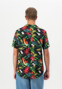 Schwarzes kurzärmeliges Hemd mit lebhaftem tropischem Blumenmuster in Rot, Orange und Weiß, kombiniert mit blauen Jeansshorts.