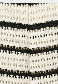 Gros plan d'un tissu tricoté blanc avec des rayures horizontales noires alternées et des motifs ajourés semblables à de la dentelle.