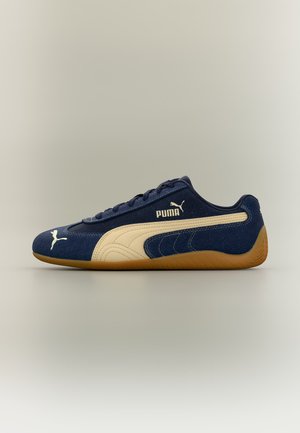 Tmavomodrá teniska Puma s béžovým pruhom a gumovou podrážkou, bočný pohľad, s logom Puma na prednej časti a boku.