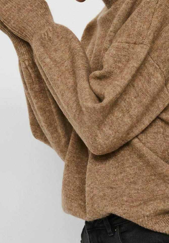 Pull en maille marron avec une finition texturée, manches longues et coupe décontractée, porté avec un pantalon noir.