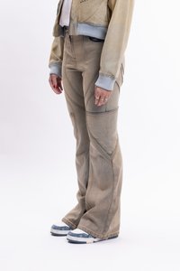 Bež flared traperice s kontrastnim šavovima i bočnim džepovima, uparene s plavim i bijelim tenisicama, prikazane protiv bijele pozadine.