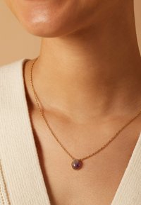 Gouden kettinghalsketting met een ronde paarse edelsteenhanger, met een gladde textuur, delicate schakels en een ovale vorm.