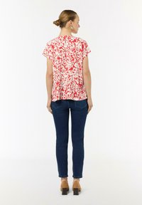 Rot-weiße blouse mit kurzem Ärmel, lockerer Passform und einem Schlüsselloch-Design im Rücken, kombiniert mit blauen Skinny Jeans und beigen High Heels.