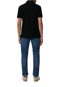 Czarna koszulka polo z kołnierzykiem, zestawiona z niebieskimi dżinsami. Model nosi beżowe sneakersy z jasną podeszwą i ciemnymi akcentami.