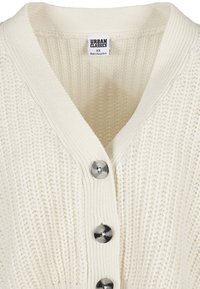 Stickad cardigan i off-white med V-hals och fem knappar. Den texturerade tyget har en ribbad design med en slät finish vid kragen.