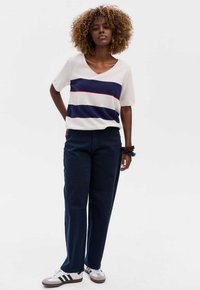 Wit en marineblauw gestreepte gebreide top met een V-hals, gecombineerd met donkerblauwe wijde broek en grijze sneakers met zwarte strepen. Casual pasvorm.