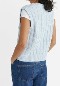 Hellblauer gestrickter ärmelloser Pullover mit Zopfmuster, versehen mit einem gerippten Saum, kombiniert mit blauen Denim-Jeans.