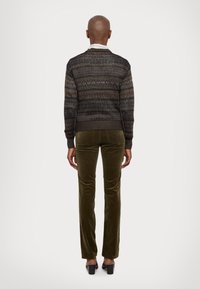 Knit sweater in dark tones with multicolored patterns, paired with olive green velvet pants, featuring a tailored fit. Black high-heeled shoes.