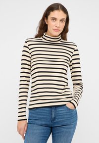 Gestreiftes Rollkragenoberteil in Beige und Schwarz mit geripptem Textureffekt und langen Ärmeln, kombiniert mit blauen Jeans.