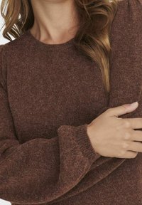 Maglione marrone lavorato a maglia con scollo rotondo e tessuto testurizzato. Maniche a vestibilità ampia, leggera variazione di colore e polsini a coste.