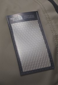 Le logo The North Face et le texte "Never Stop Exploring" sur un patch à motif hexagonal cousu sur un tissu vert olive.