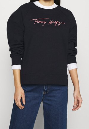 Felpa nera con vestibilità rilassata, dotata di maniche raglan e logo ricamato "Tommy Hilfiger" rosso sul petto. Materiale in cotone.