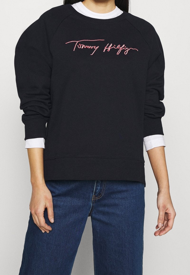 Felpa nera con vestibilità rilassata, dotata di maniche raglan e logo ricamato "Tommy Hilfiger" rosso sul petto. Materiale in cotone.